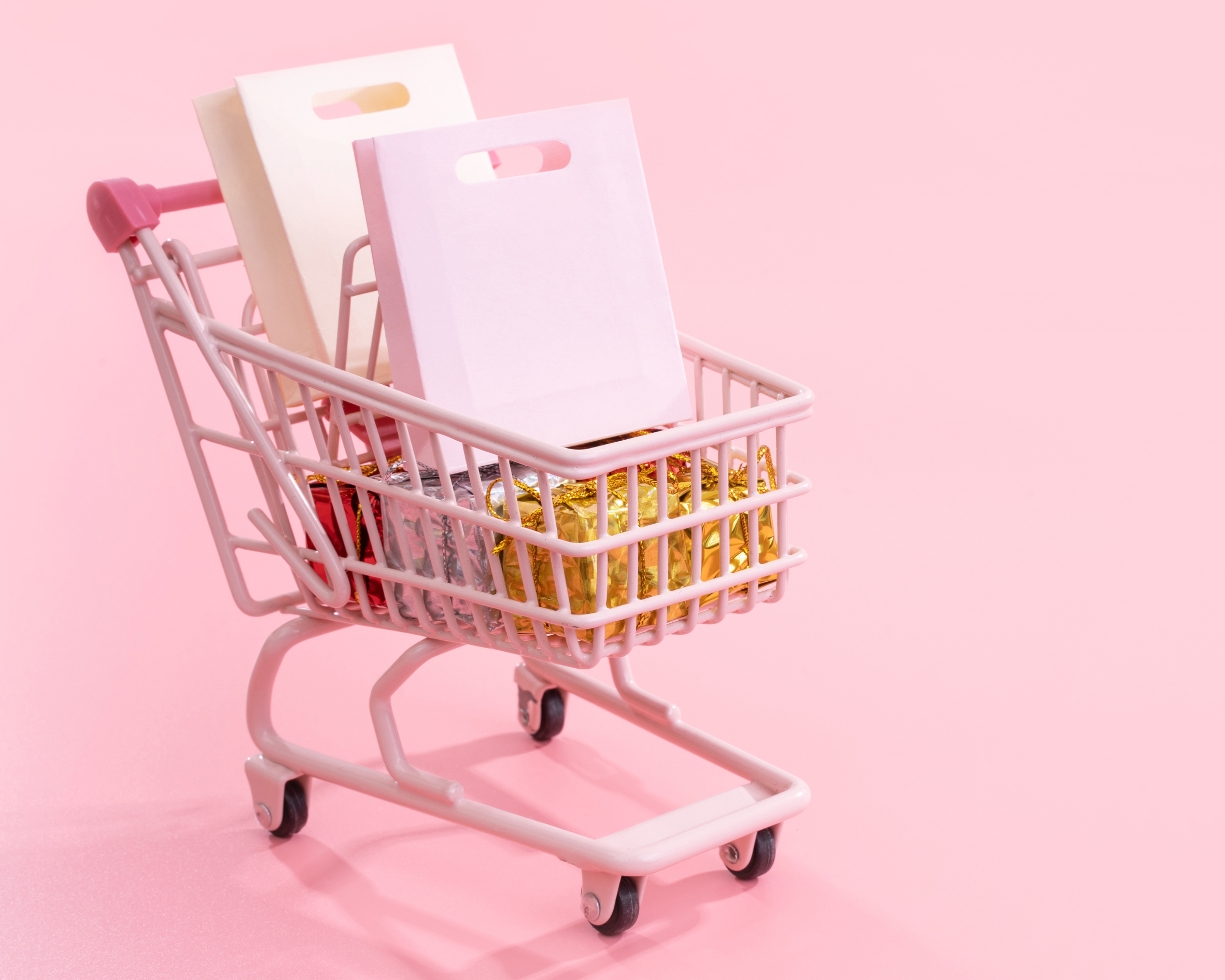 Small shopping cart filled with colorful books on a pink background